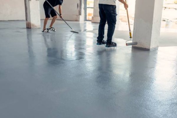 Two construction workers applying grey epoxy resin in an industrial hall